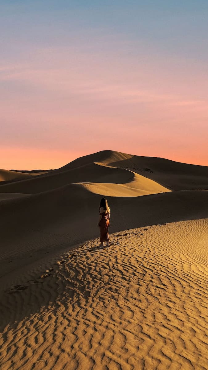 woman in black dress walking on desert during daytime
