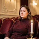 Jeune femme écoutant une bande originale de film lors d'un concert candlelight dans une salle de cinéma vintage aux fauteuils en velours rouge
